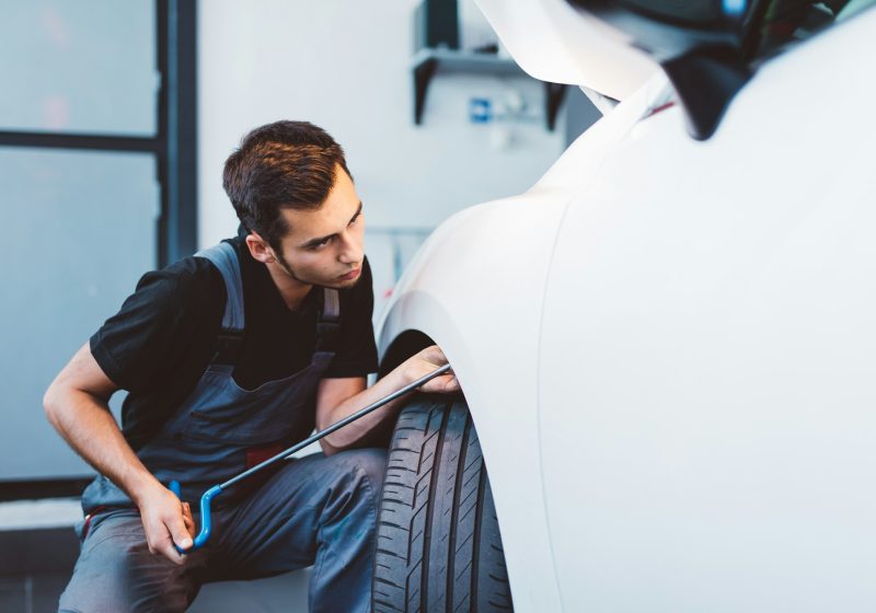 Car mechanic working to remove dent in workshop.