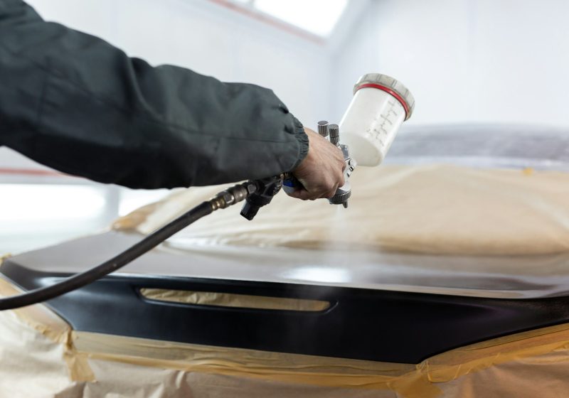 Close-up of a spray gun with black paint for painting a car in a special booth