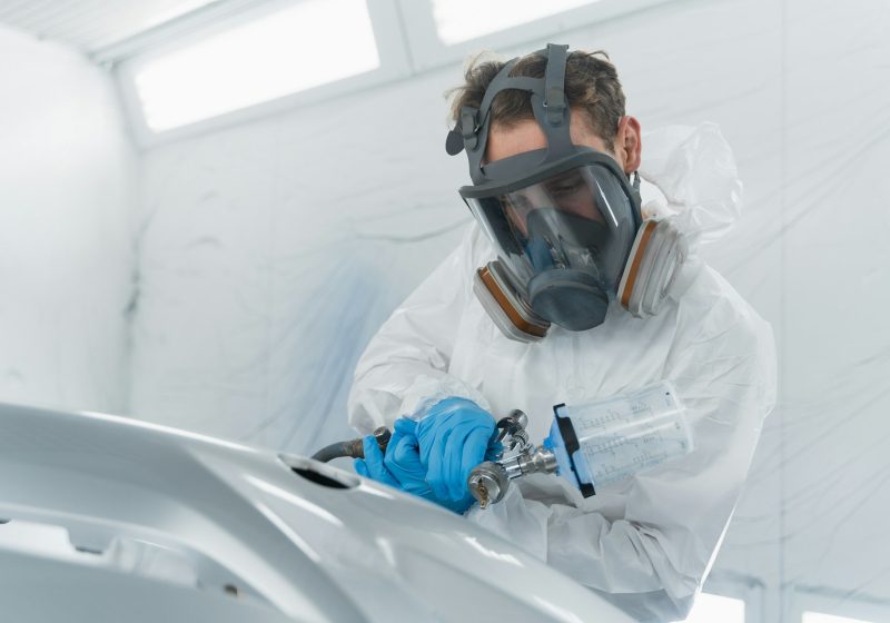 Car painter applies a layer of varnish to the surface of a car bumper.